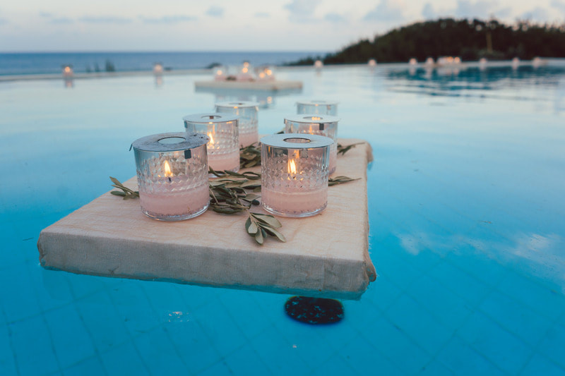 Peaceful view of candles floating on top of plank in a Sparkling Clean Pool with a view of the ocean in the background.