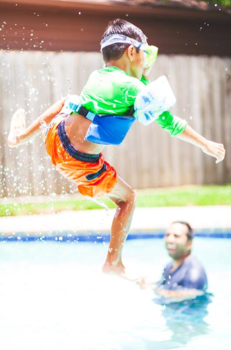 Boy jumping into in ground pool and playing with dad